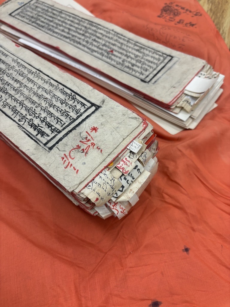 The photo is a closeup of a traditional Tibetan text with scraps of paper tucked inside to take notes.