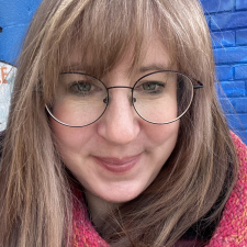 Woman with bangs and glasses standing in front of a blue background
