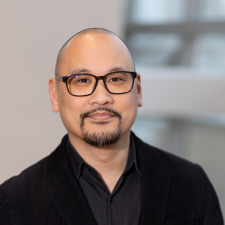 headshot of Glen Morales, a bald man with dark glasses and a goatee, wearing a black shirt and black blazer. 